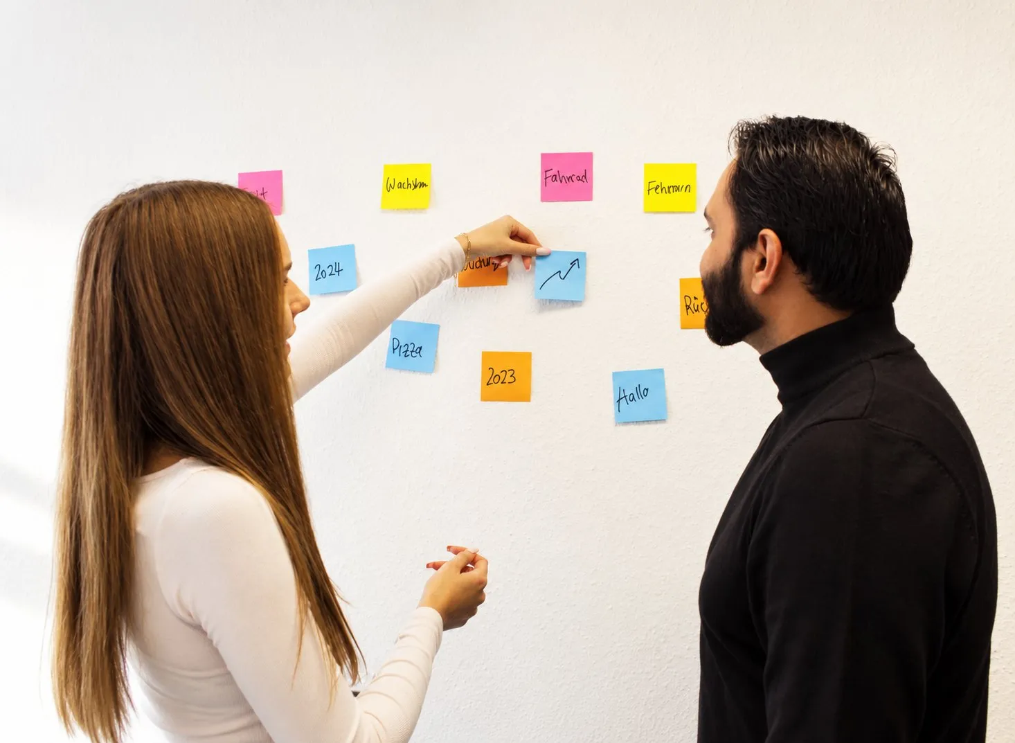 Zwei Teammitglieder sortieren Ideen auf Post-its an der Wand